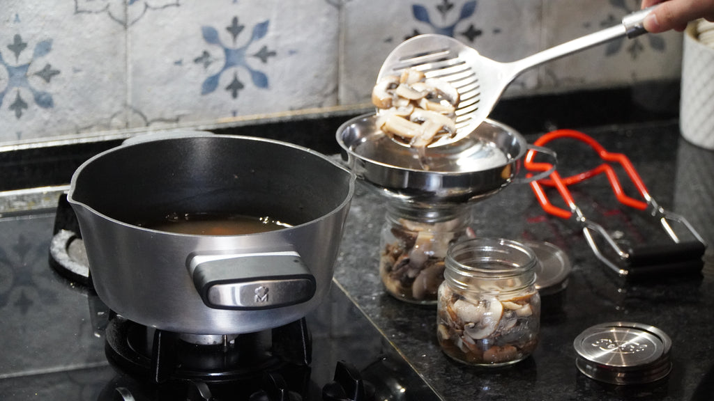 Stove with pot, jars of food, and cooking utensils on a tiled backsplash.