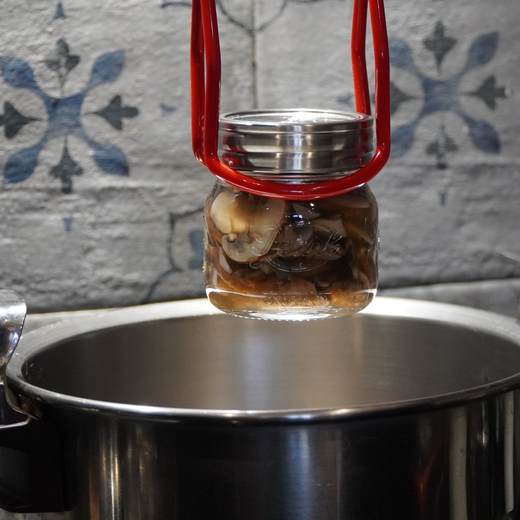 Jar with a red lid on top of a metal pot against a tiled wall background